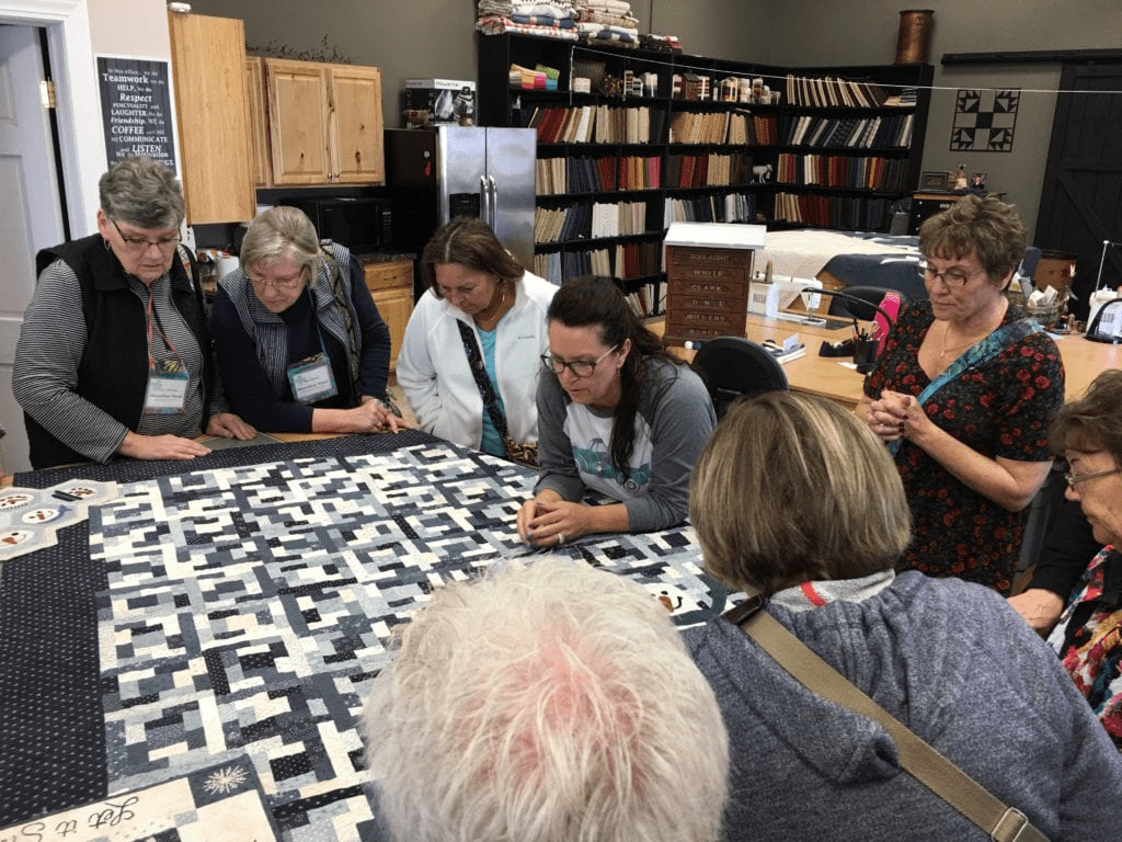 A group of people sitting around a table with a quilt.